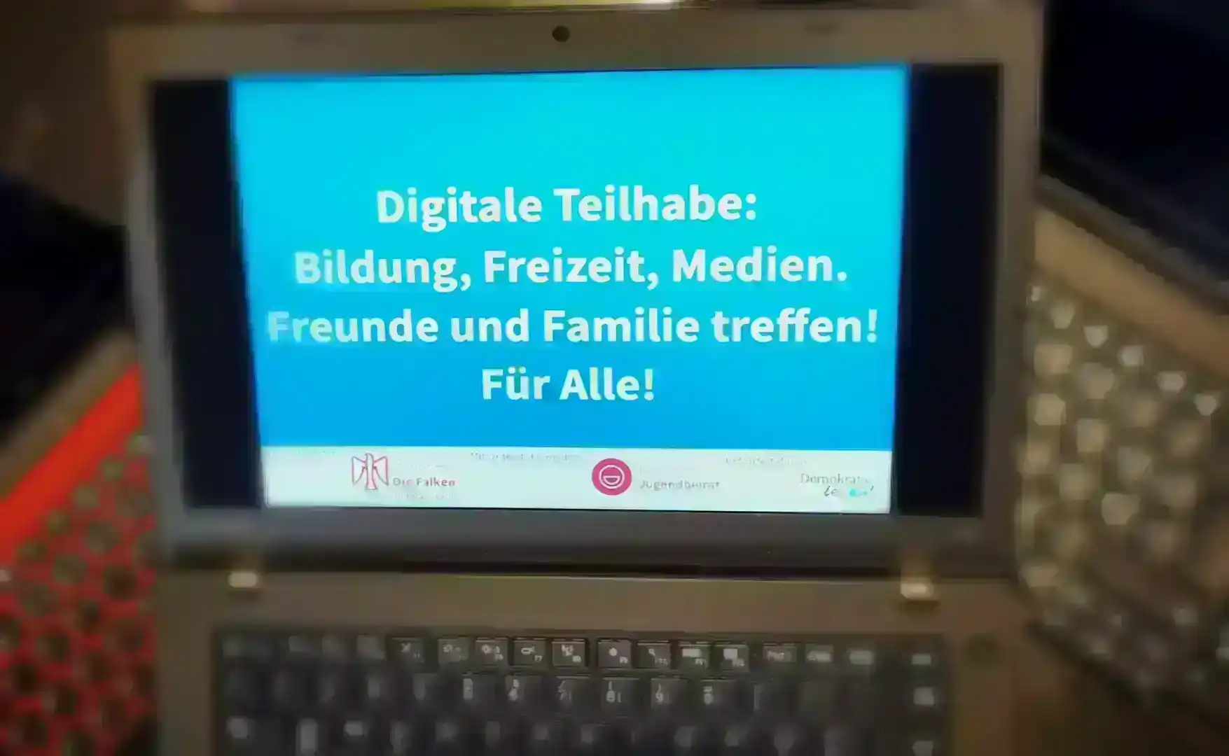 Laptop mit Bildschirmaufschrift Digitale Teilhabe: Bildung, Freizeit, Medien. Freunde und Familie treffen! für Alle! Unterstützer: SJD - Die Falken Mannheim, 68deins! Jugendbeirat. Gefördert von „Demokratie Leben“